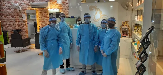 Staff at Glowup Studio in protective gowns, face shields and masks, standing at the reception counter beside the salon logo.